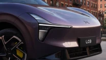 Przedni fragment futurystycznego samochodu elektrycznego w fioletowym kolorze, z wyrazistymi reflektorami LED, czarną tablicą rejestracyjną z napisem LO3 i żółtym zaciskiem hamulcowym widocznym przez nowoczesną felgę.