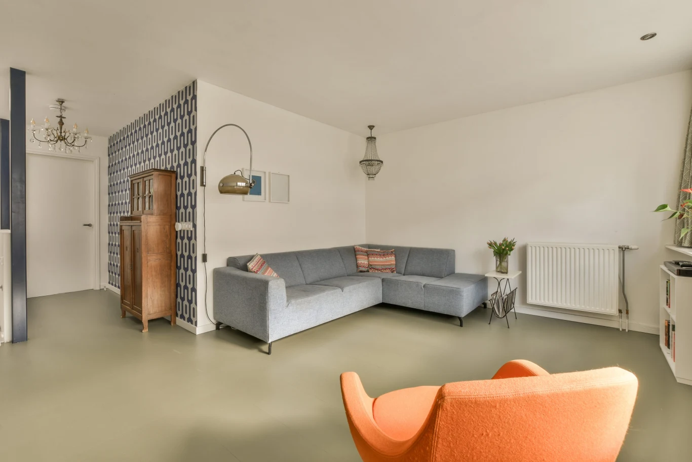 a living room with an orange chair in the middle and a blue couch on the other side, next to it Salon z podłogą z mikrocementu.