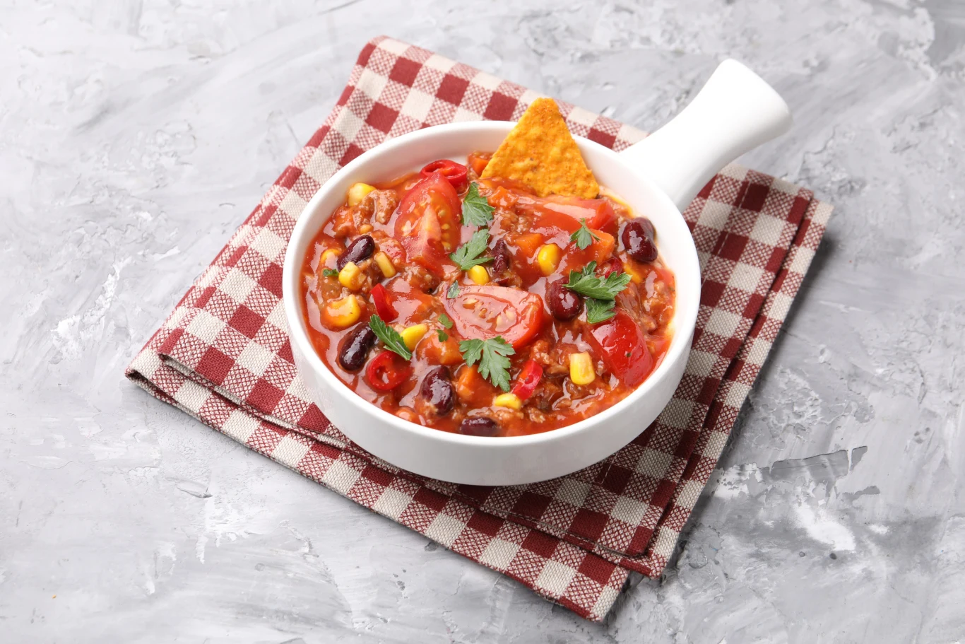 Większość Polaków o tym nie wie. Kostka czekolady potrafi odmienić chili con carne Miska chili con carne z czerwoną fasolą, kukurydzą, pomidorami, papryką, kolendrą i nachosem na serwetce w kratkę.