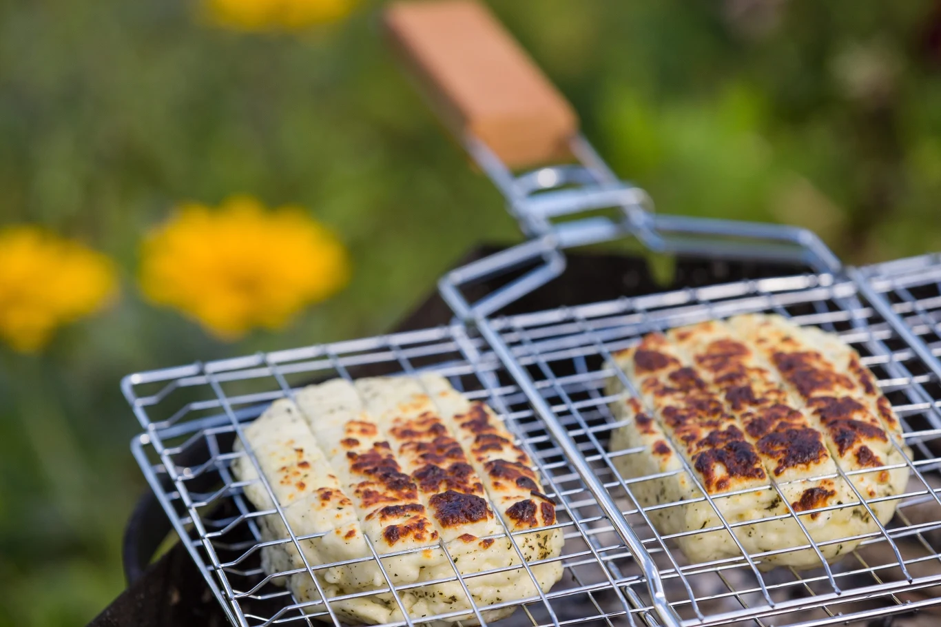Dwie porcje sera z wyraźnymi śladami grillowania, umieszczone w metalowym ruszcie do grilla.