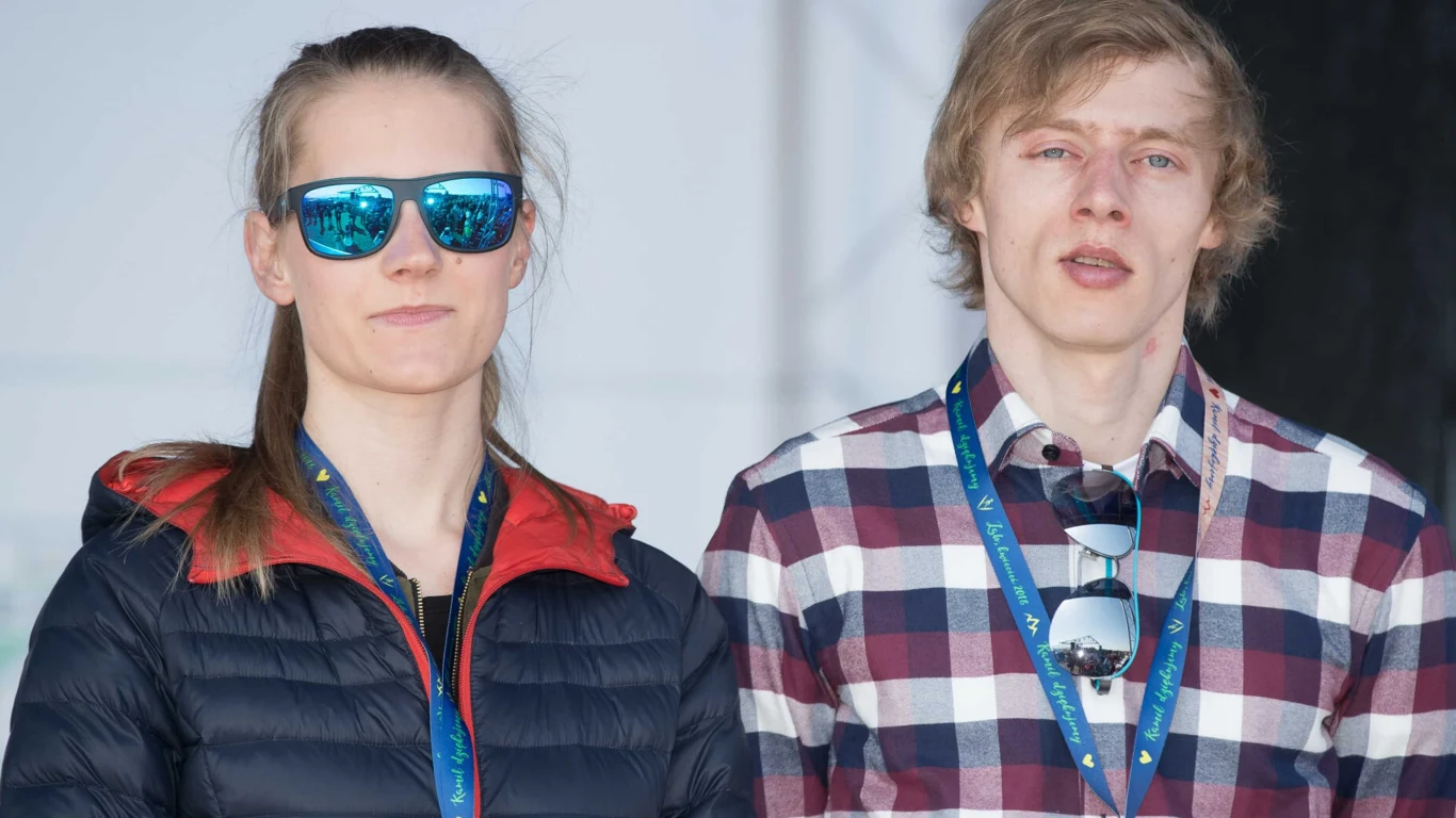 Marta Kubacka, Dawid Kubacki Dwie młode osoby z identyfikatorami na szyi, jedna w ciemnych okularach przeciwsłonecznych i sportowej kurtce, druga w koszuli w kratę, stoją obok siebie patrząc w stronę obiektywu.
