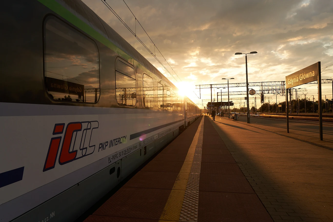 Nowoczesny pociąg pasażerski PKP Intercity zatrzymany przy peronie na stacji Gdynia Główna oświetlony ciepłym światłem zachodzącego słońca.