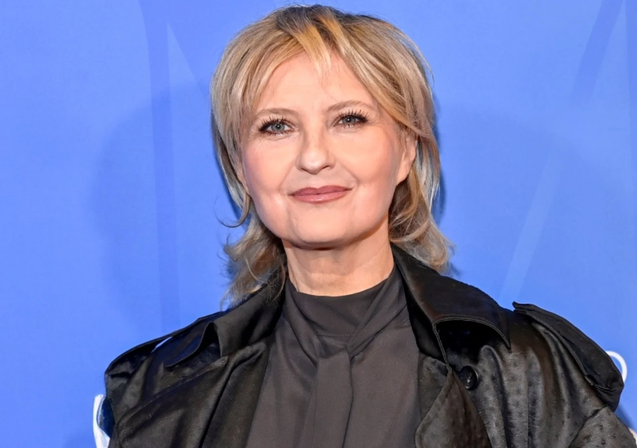Izabela Kuna Izabela Kuna na niebieskim tle, ubrana w czarną marynarkę i transparentną koszulę.