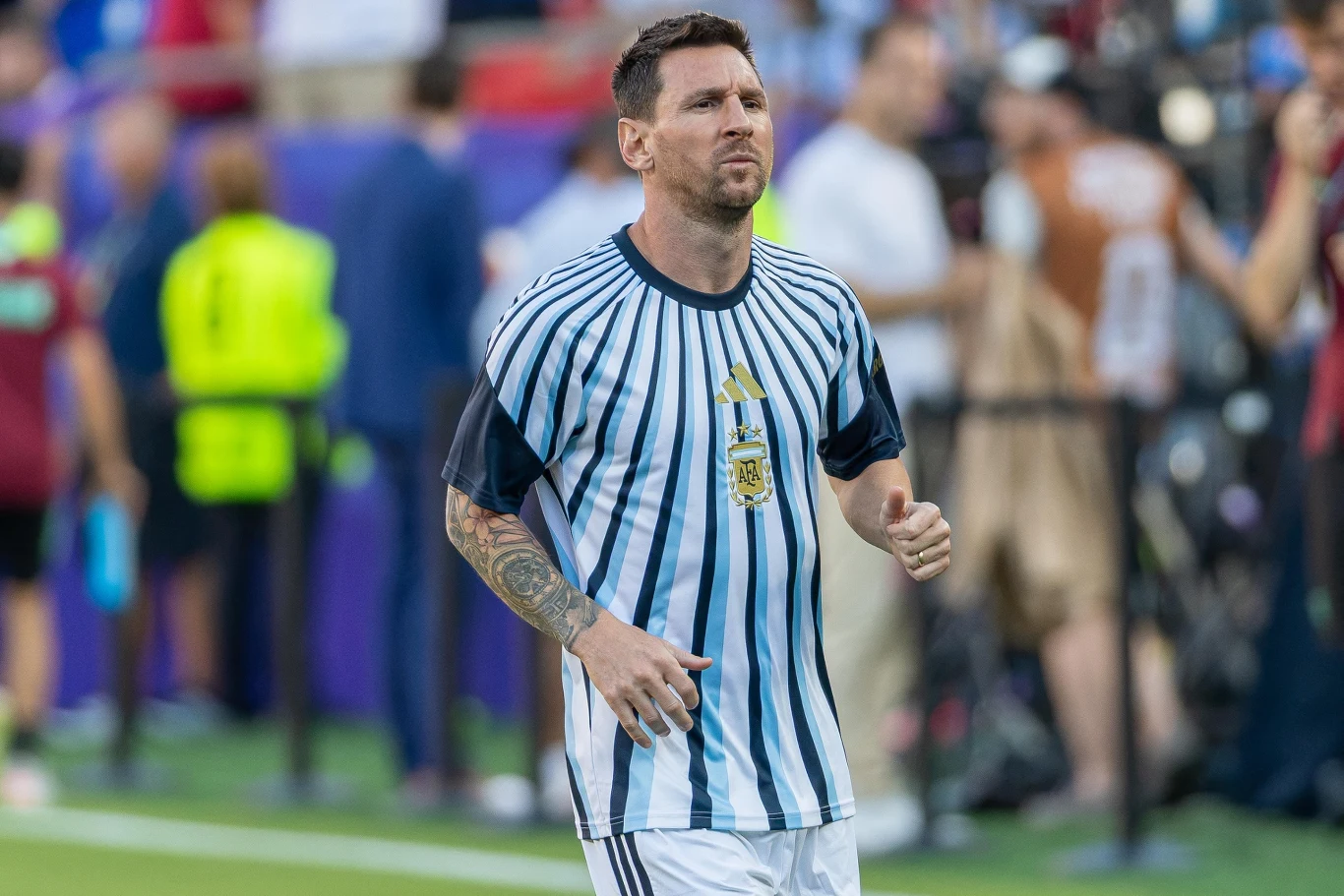 Leo Messi Piłkarz w biało-niebieskiej koszulce z herbem Argentyny biegnie po boisku, w tle rozmazane sylwetki ludzi na trybunach.
