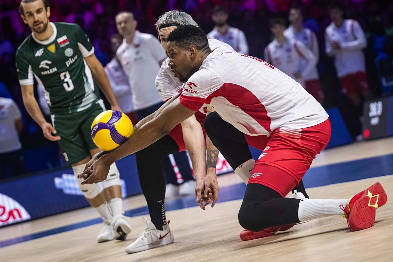 Siatkarz w biało-czerwonym stroju odbija piłkę podczas meczu, koncentrując się na precyzyjnym przyjęciu, w tle widoczni inni zawodnicy w sportowych strojach.