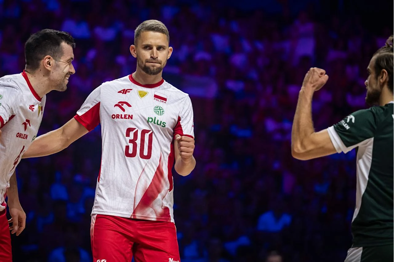 Dwóch siatkarzy w biało-czerwonych koszulkach drużyny Polska oraz przeciwnik w zielonym stroju podczas sportowej rywalizacji na hali przy świetle scenicznych reflektorów.