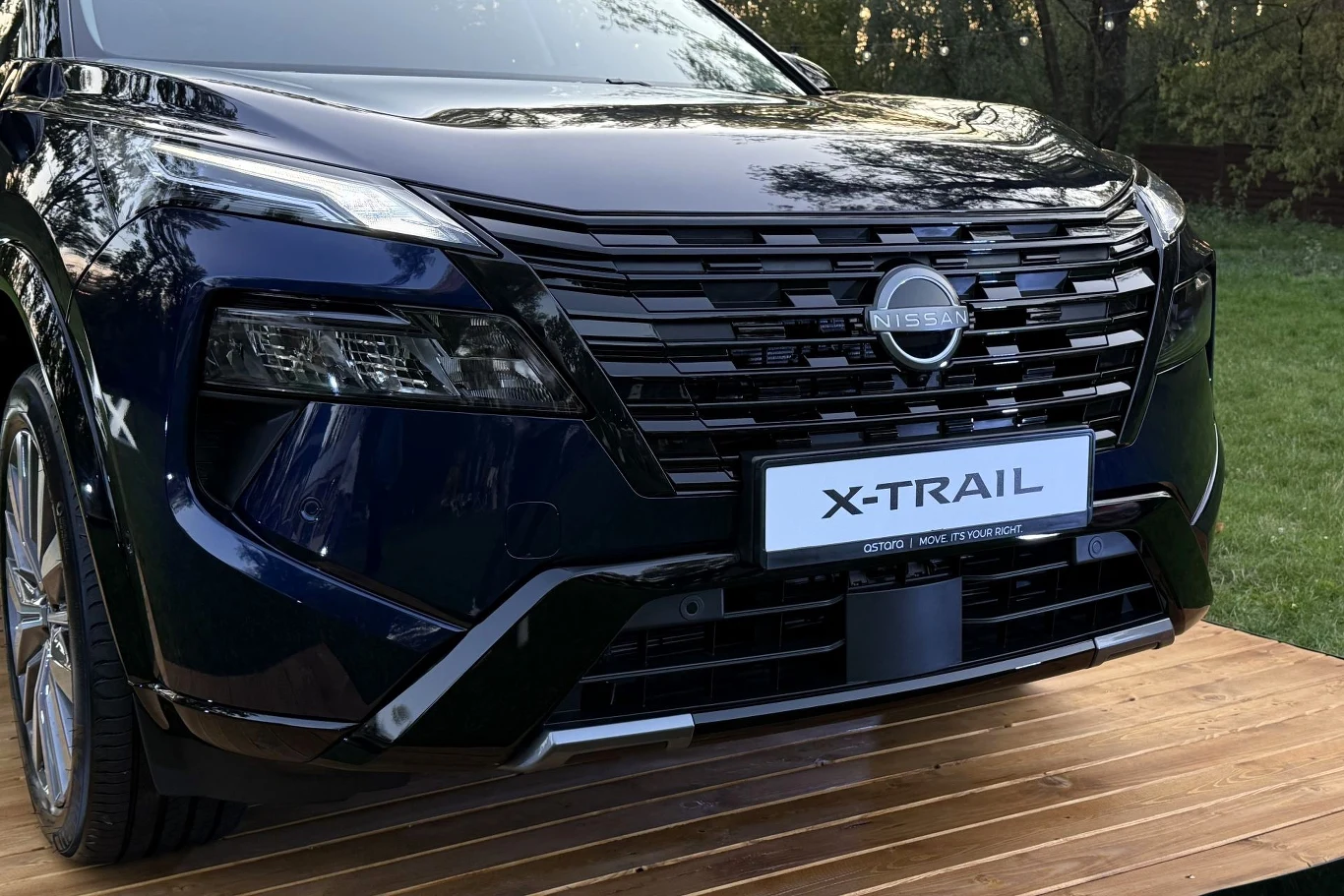 Ciemnogranatowy przód Nissan X-Trail z charakterystycznym dużym grillem, agresywnie zarysowanymi reflektorami LED oraz wyraźnym logo marki na masce.
