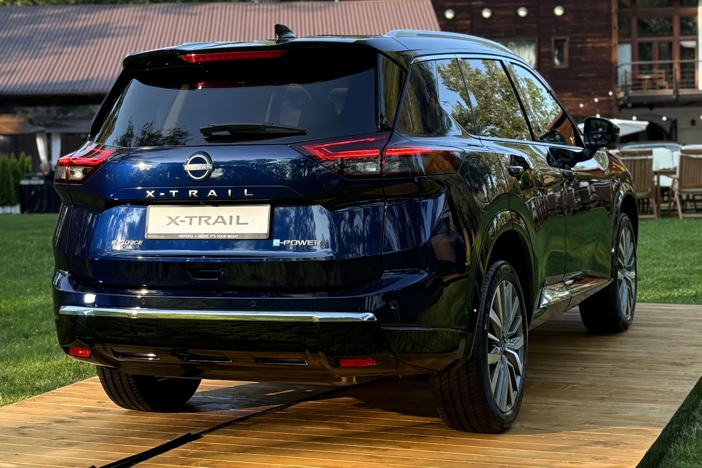 Niebieski Nissan X-Trail ustawiony na platformie drewnianej, widoczny tył auta z charakterystycznymi lampami LED, chromowanymi detalami oraz oznaczeniem modelu.