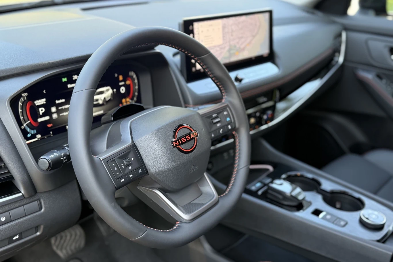 Nowoczesna deska rozdzielcza samochodu Nissan z cyfrowym zestawem wskaźników, dużym ekranem nawigacji oraz wielofunkcyjną kierownicą ozdobioną czerwonym logotypem marki.