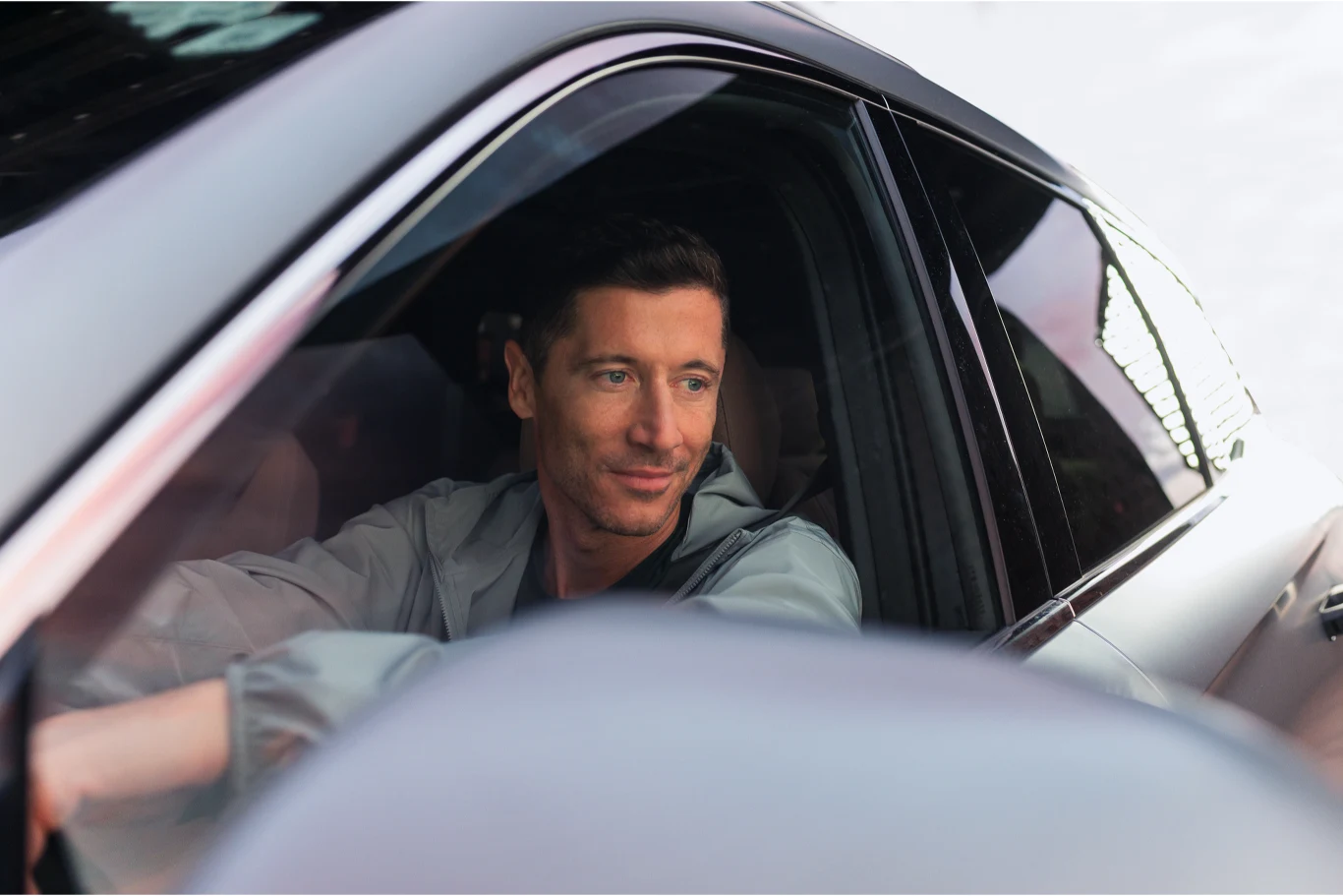 Robert Lewandowski wystąpił w reklamie Chery. Robert Lewandowski za kierownicą ciemnego samochodu Chery, patrzy przez boczne okno.