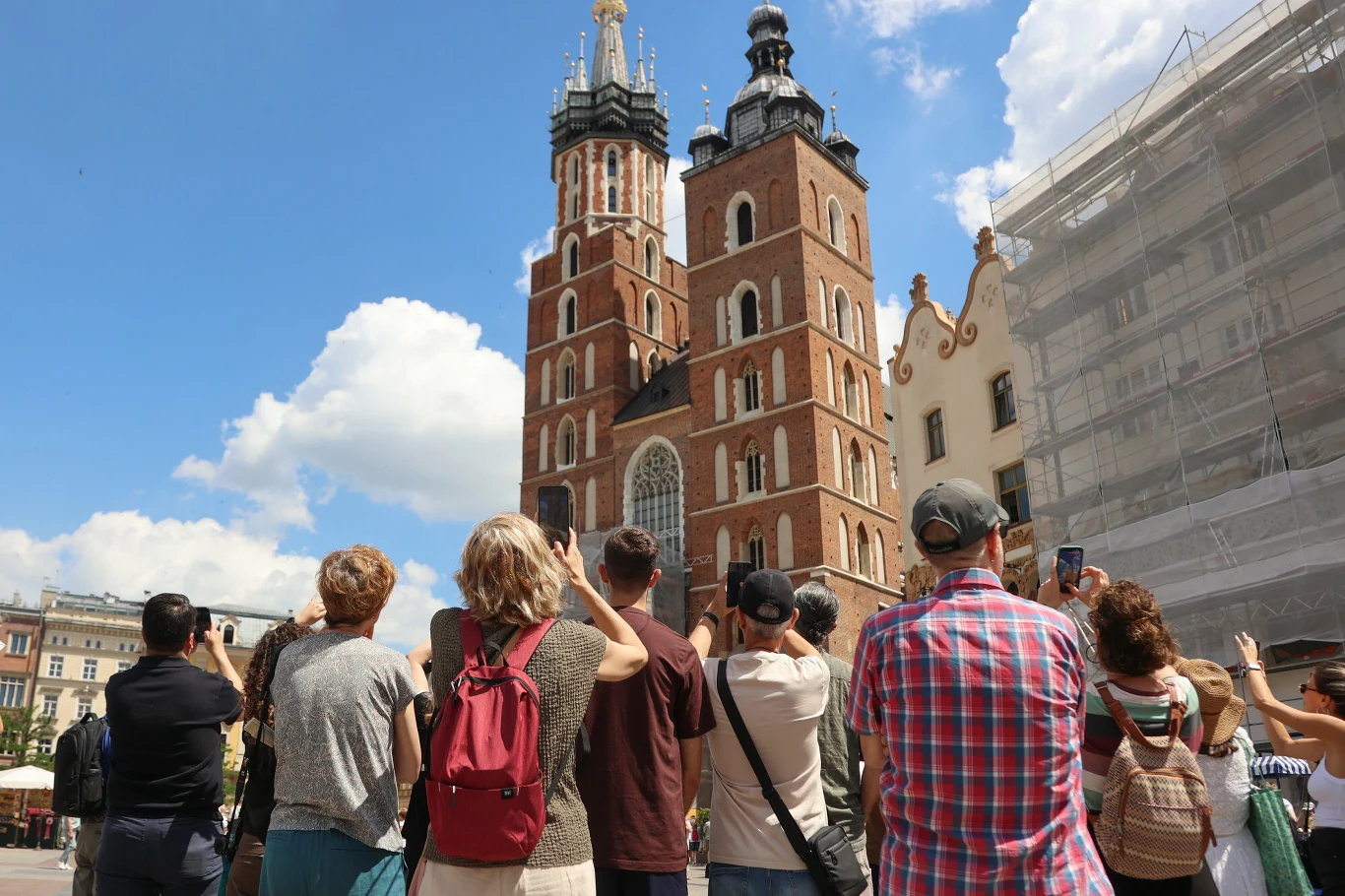Kraków odwiedza rocznie ponad 16 milionów osób. Mieszkanka Aleksandra mówi: "To nie UNESCO odpowiada za problemy związane z turystyfikacją" Grupa turystów zwrócona w stronę kościoła Mariackiego w Krakowie, podziwiających i fotografujących charakterystyczne, dwie nierówne wieże tej gotyckiej świątyni.