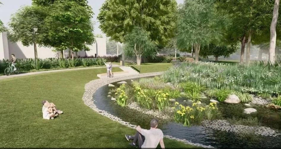 Zielony park z niewielkim stawem, licznymi drzewami i krzewami oraz ścieżką spacerową, wśród której wypoczywa kilka osób na trawie.