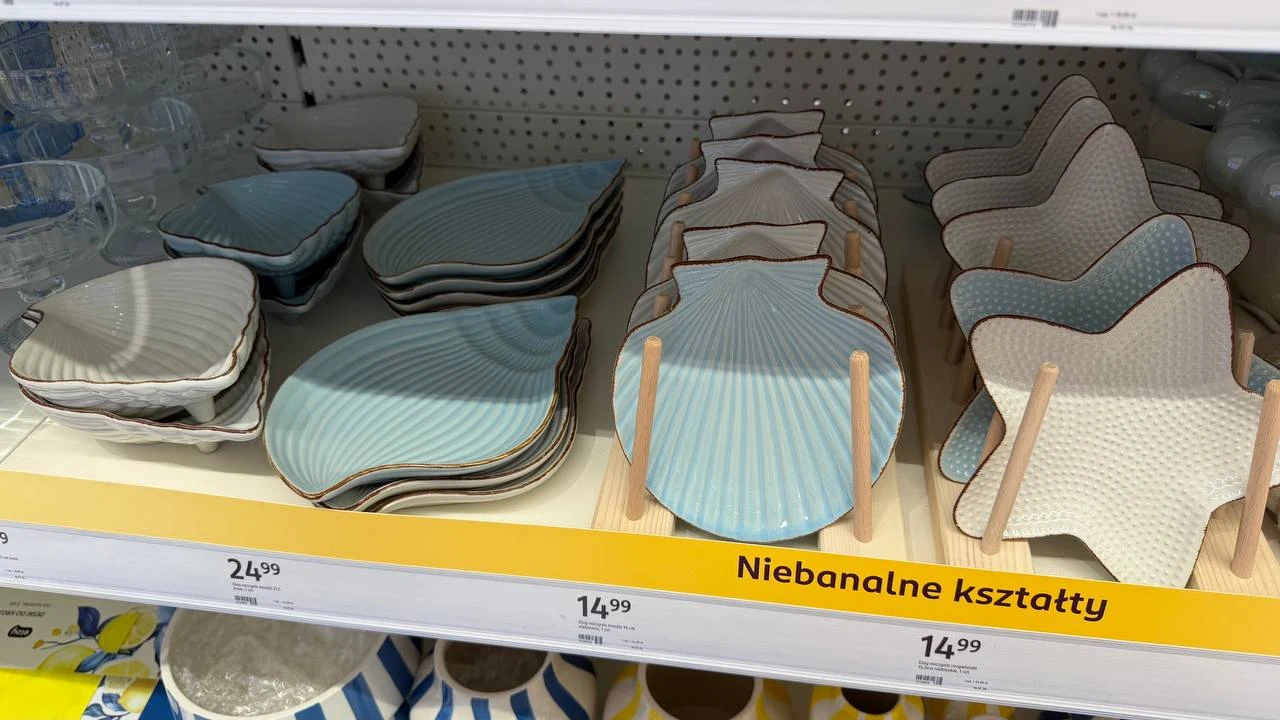 Zestaw ceramicznych talerzy i półmisków w niebanalnych, organicznych kształtach oraz stonowanych kolorach, ustawionych na półce sklepowej obok siebie.