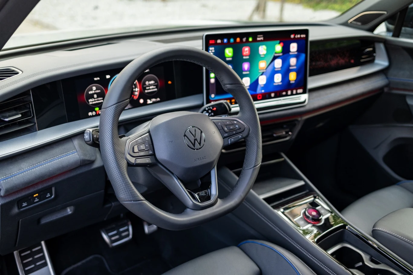 Nowoczesna deska rozdzielcza Volkswagena z dużym, poziomym ekranem dotykowym prezentującym aplikacje, cyfrowy panel wskaźników, wielofunkcyjna kierownica oraz minimalistyczna konsola środkowa z elektronicznym wybierakiem biegów.