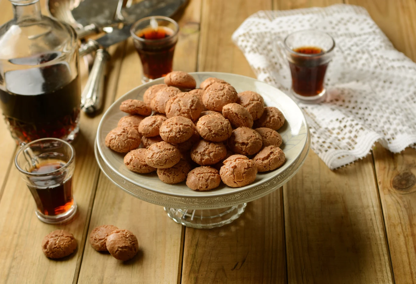 Nie ma lepszego dodatku do kawy Stos ciasteczek amaretti na szklanej paterze, trzy kieliszki z ciemnym likierem i karafka na drewnianym stole.