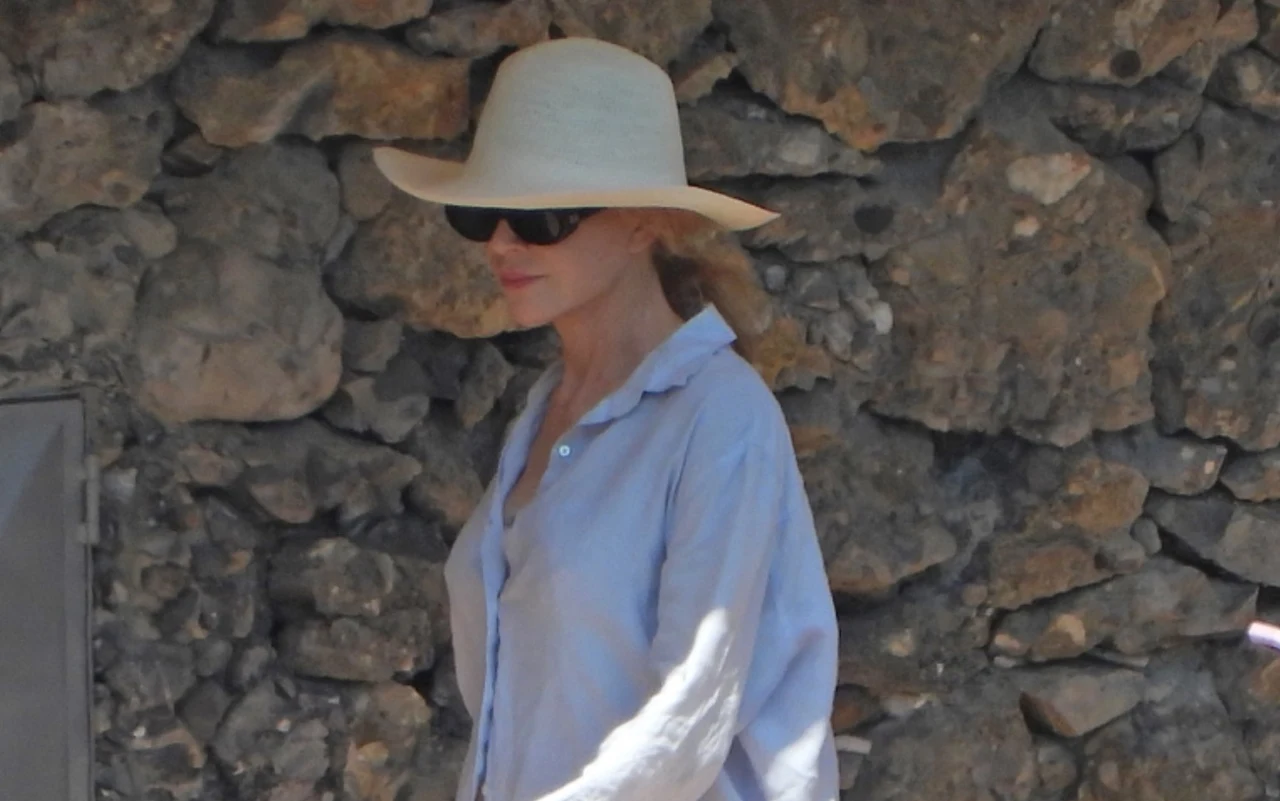 Naturalna Nicole Kidman wypoczywa w Portofino Nicole Kidman w kapeluszu i okularach przeciwsłonecznych, w jasnej koszuli, stoi na tle kamiennego muru w Portofino.