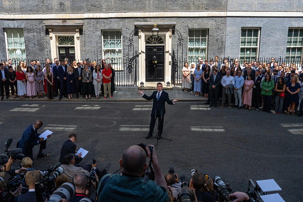 Andy Burnham podczas pierwszego dnia urzędowania na Downing Street Andy Burnham przemawia do mediów przed budynkiem Downing Street, widoczne czarne drzwi i oficjalne osoby w tle.