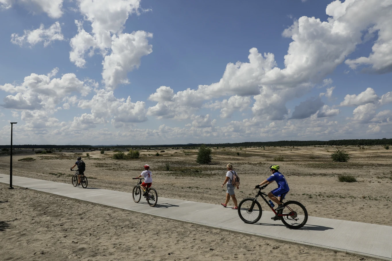 Popularnością cieszy się też trasa wokół Pustyni Błędowskiej Czwórka osób poruszających się ścieżką rowerową na tle rozległego, piaszczystego terenu i nieba pełnego chmur; trzech z nich jedzie na rowerach, jedna osoba idzie pieszo.