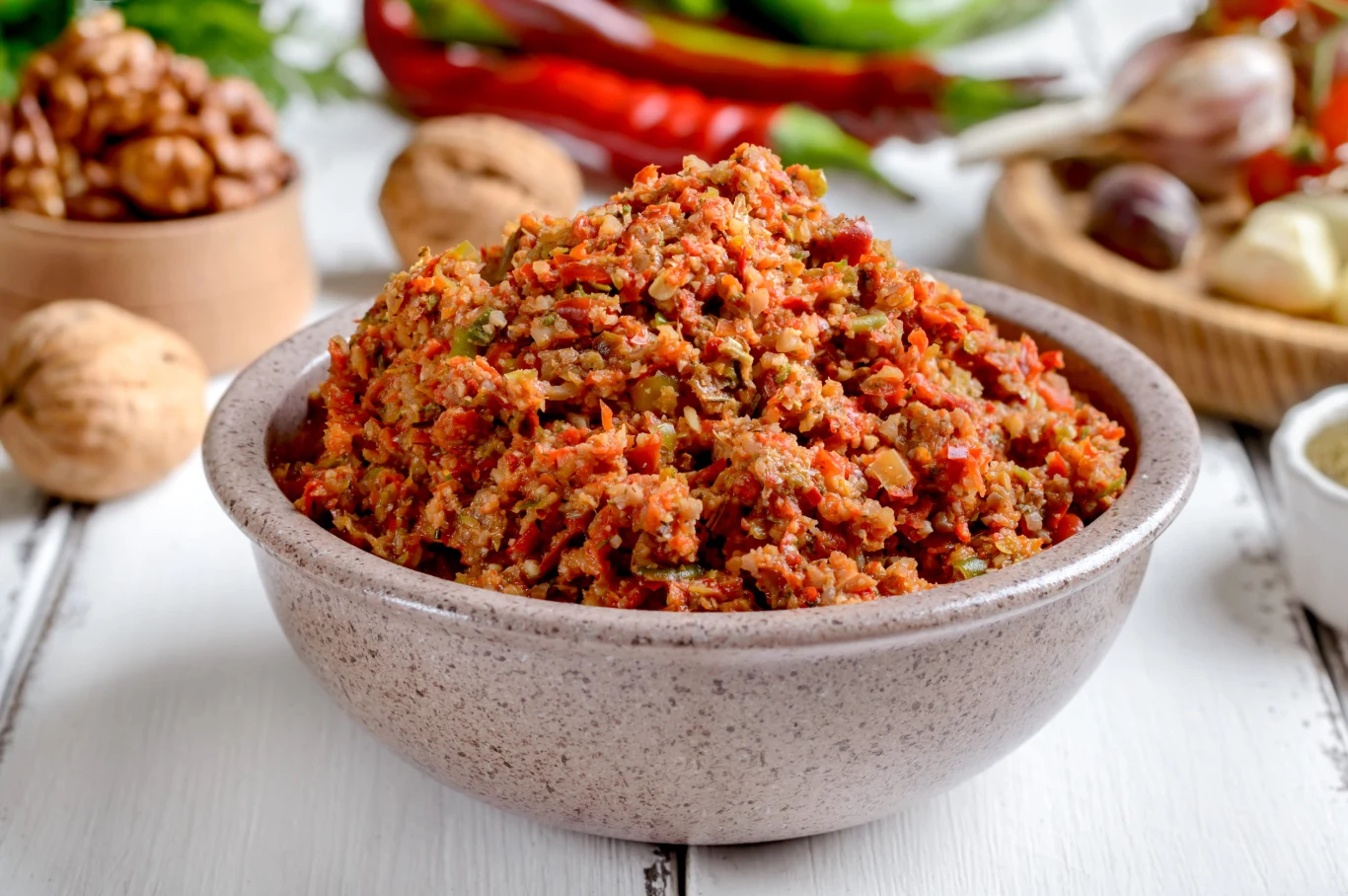 Adjika to pełna smaku gruzińska pasta, którą można dodać do wielu dań Miska z gruzińską pastą adjika z posiekanych orzechów włoskich, papryki i przypraw na jasnym blacie.