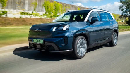 Granatowy SUV z nowoczesnym wzornictwem porusza się po jezdni, podkreślony zielonymi tablicami rejestracyjnymi i dużymi aluminiowymi felgami.