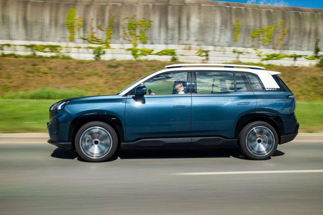 Niebieski samochód typu SUV jadący po asfaltowej drodze, za kierownicą siedzi dorosła osoba.
