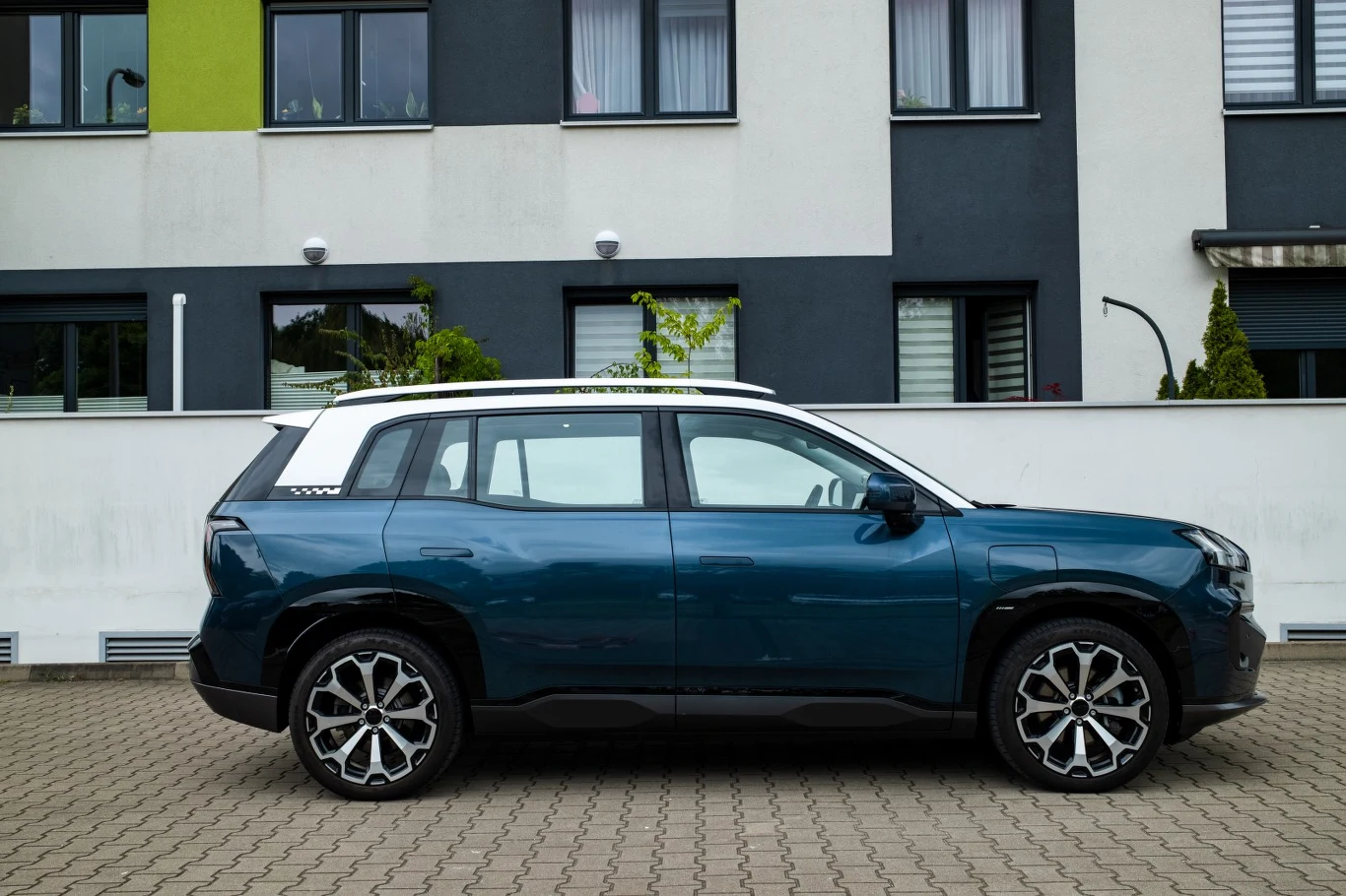 Granatowy SUV z białym dachem zaparkowany na kostce brukowej, w tle nowoczesny budynek mieszkalny o szaro-białej elewacji.