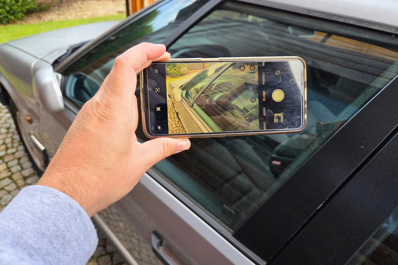 Samo wykonanie zdjęcia radia przez kontrolera nie oznacza, że nałożony zostanie mandat. Dłoń trzymająca smartfon z wyświetlonym na ekranie obrazem odbicia samochodu w szybie bocznej pojazdu.