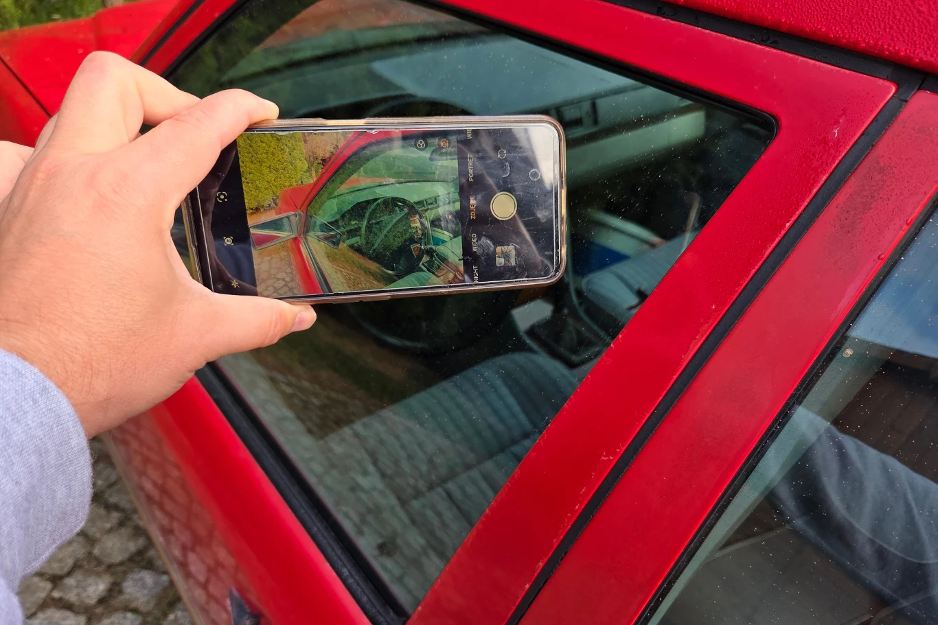 W Polsce pracuje aktualnie 24 kontrolerów. Mówienie o masowych akcjach przeciwko zmotoryzowanym jest mocno na wyrost. Telefon komórkowy skierowany na szybę czerwonego samochodu, na ekranie widoczny odbity obraz wnętrza pojazdu z kierownicą i deską rozdzielczą.