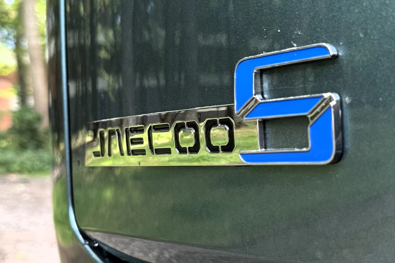 Jaecoo 5 Hybrid startuje cenowo od 119 500 zł. Emblemat JMECOO 5 umieszczony na ciemnozielonym nadwoziu samochodu, litera S wyróżniona niebieskim kolorem.