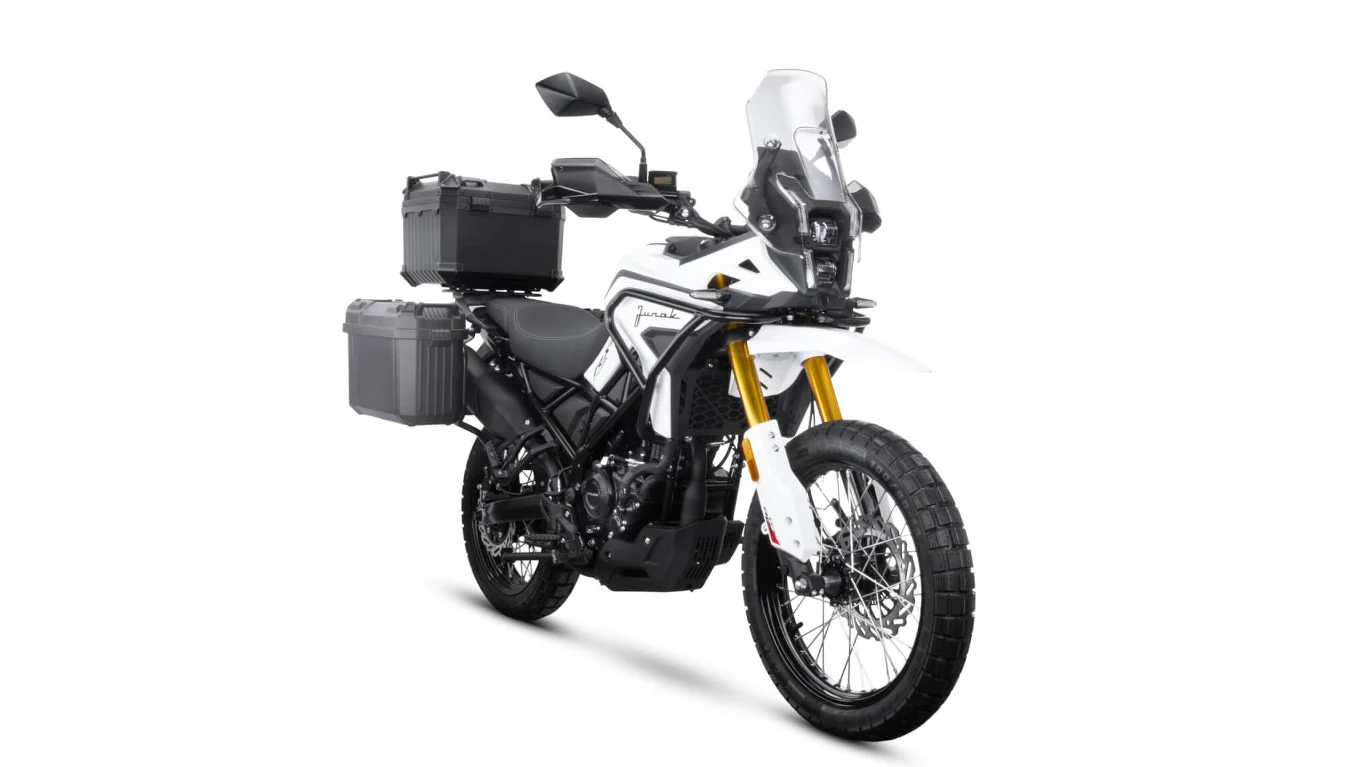Biały motocykl terenowy wyposażony w trzy pojemne kufry transportowe oraz wysoką szybę ochronną, ustawiony na białym tle.