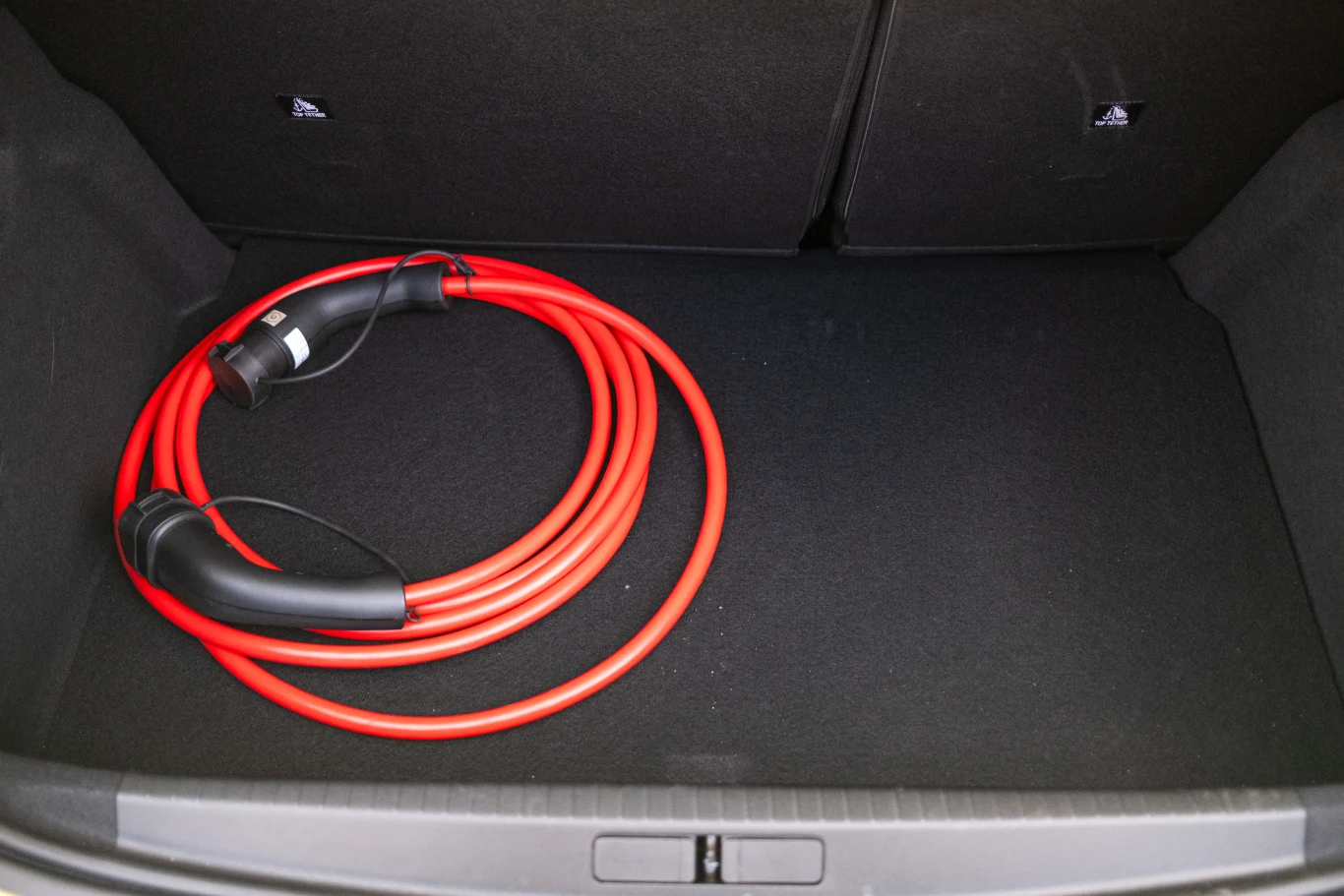 Czerwony kabel do ładowania samochodu elektrycznego ułożony na wykładzinie bagażnika.