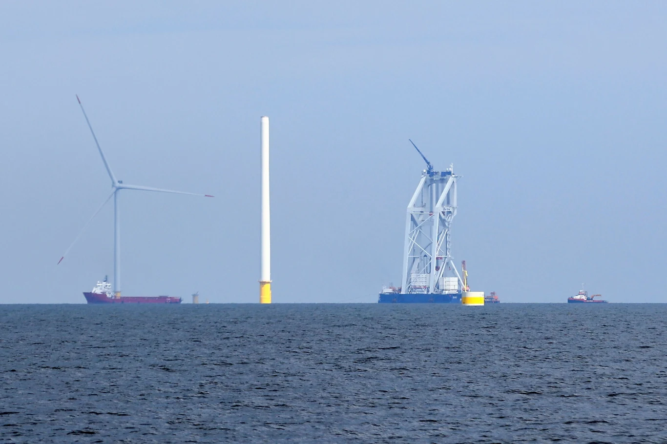 Baltic Power to oczko w głowie polskich władz Morze z kilkoma statkami, wieża wiatrowa w trakcie budowy, turbiną wiatrową oraz dużym dźwigiem pływającym pośród fal.