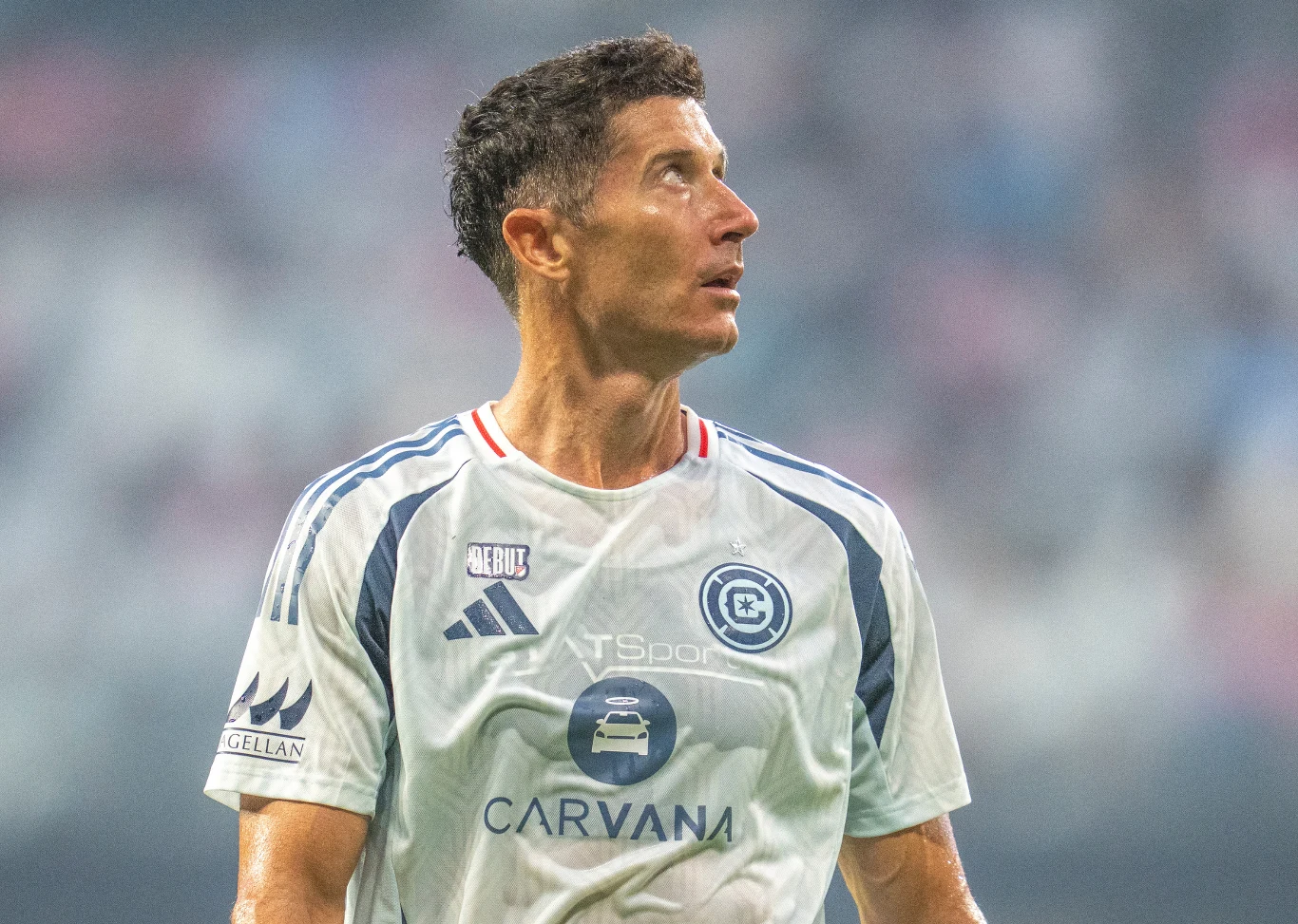 Robert Lewandowski w barwach Chicago Fire Piłkarz w białej koszulce drużyny sportowej z widocznymi sponsorami i logotypami, spoglądający w bok podczas meczu na stadionie.