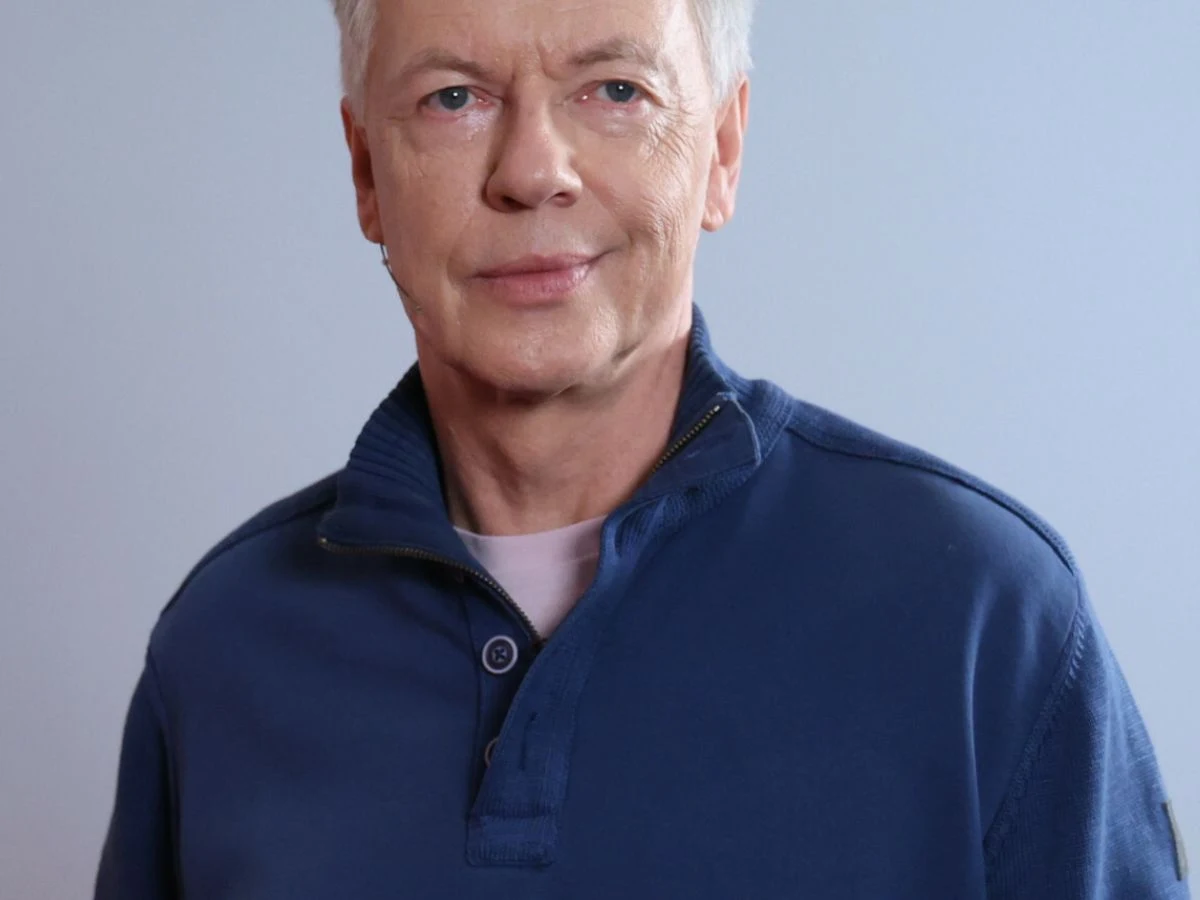 Zbigniew Suszyński Zbigniew Suszyński, aktor w niebieskiej bluzie, portretowe zdjęcie na jednolitym tle.