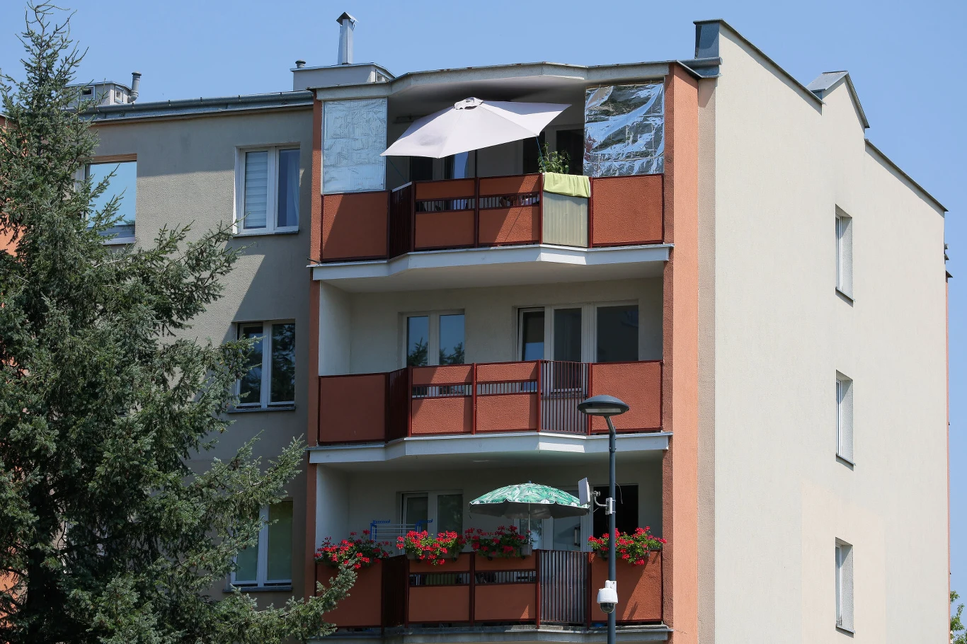 Elementy balkonów w blokach zarządzanych przez wspólnoty staną się częściami wspólnymi. Blok mieszkalny z trzema balkonami, na których stoją parasole i doniczki z kwiatami.