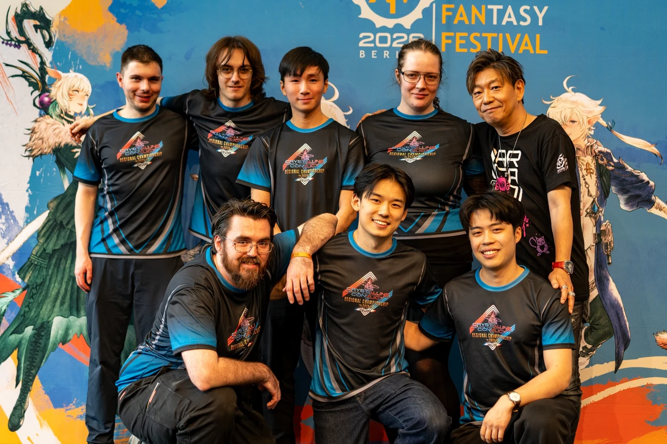Grupa siedmiu osób ubranych w jednakowe koszulki drużynowe z kolorowym logo pozuje wspólnie na tle plakatu z motywem fantasy i napisem „Fantasy Festival 2024” w jaskrawych kolorach.