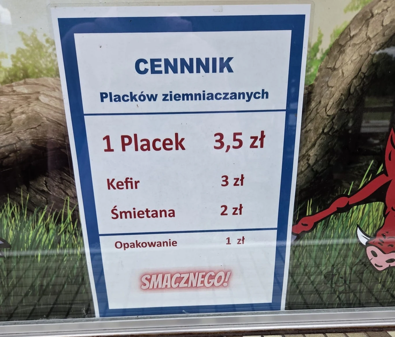 Cennik placków ziemniaczanych z cenami za jeden placek, kefir, śmietanę oraz opakowanie, umieszczony w niebieskiej ramce z dużym napisem 'SMACZNEGO!' na dole.