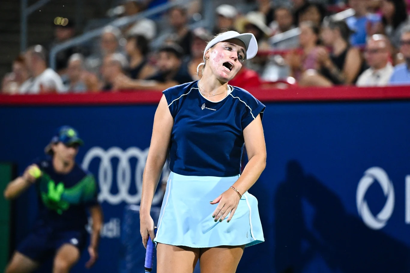 Sofia Kenin Zawodniczka tenisowa w sportowym stroju z wyrazem zmęczenia lub frustracji na twarzy, trzymająca rakietę podczas meczu na korcie, w tle widownia.