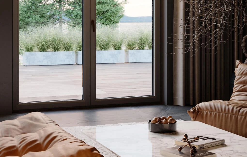 We współczesnej architekturze wyraźnie zaznacza się inny nurt - określany jako „quiet luxury" Elegancki salon z marmurowym stolikiem, na którym leżą drewniana taca z orzechami i książka, duże szklane drzwi prowadzące na taras z betonowymi donicami pełnymi zielonych traw.