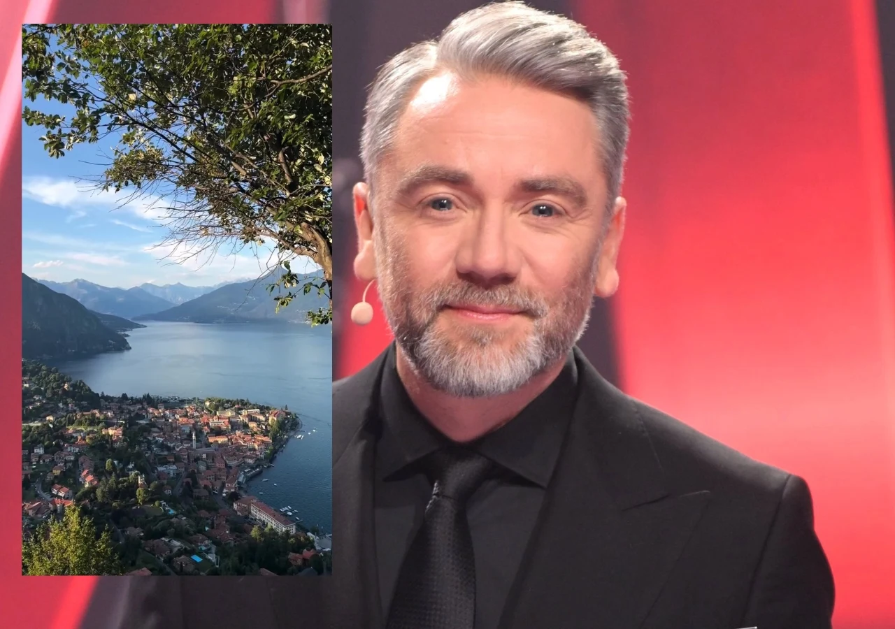 Mężczyzna z siwą brodą i włosami w eleganckim, czarnym garniturze na tle czerwonej scenografii, obok zdjęcie przedstawiające malownicze jezioro otoczone górami i niewielkim, zabudowanym miasteczkiem.