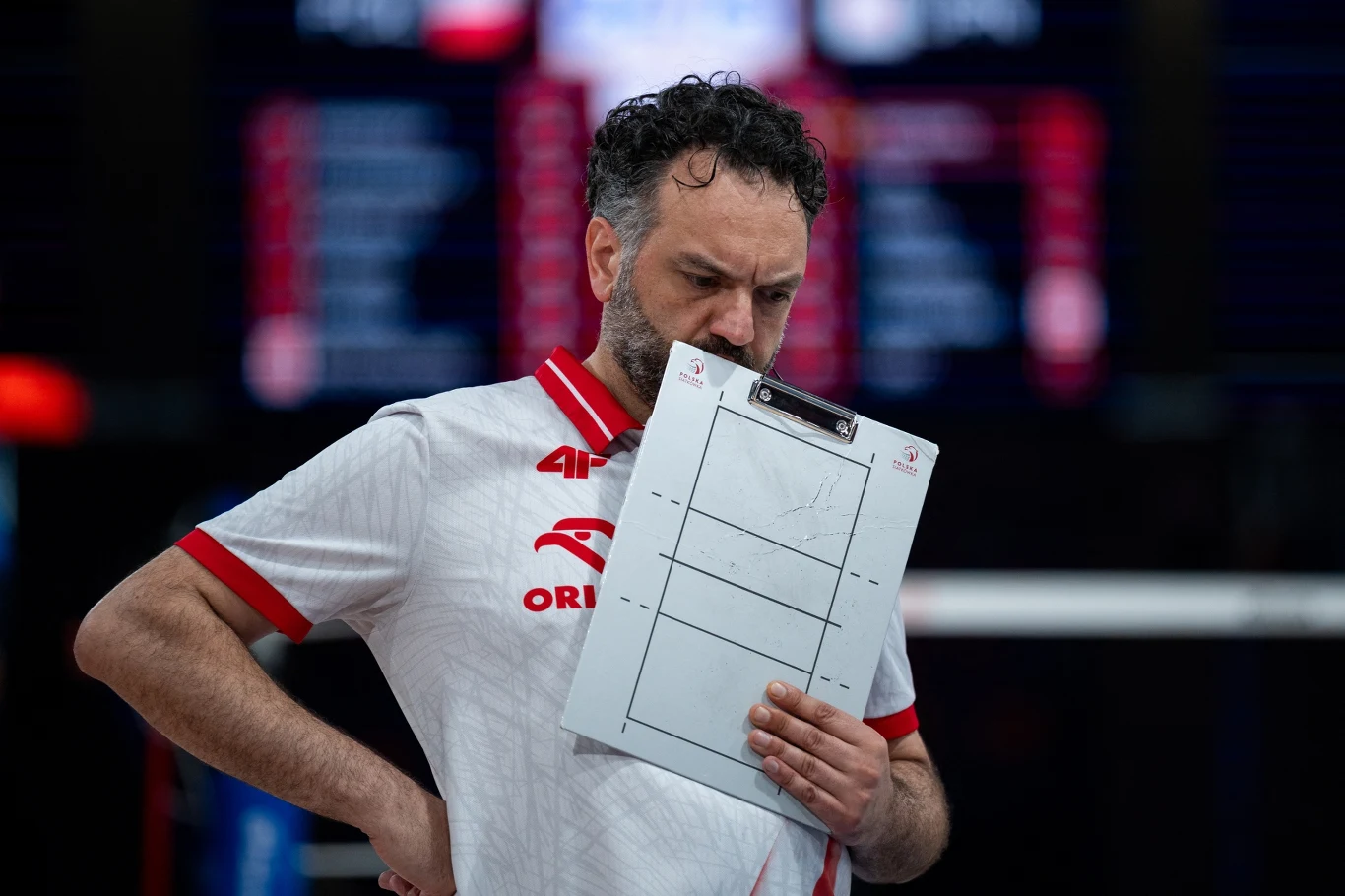 Stefano Lavarini Mężczyzna w sportowej koszulce z logo Orlen analizujący taktyczną tablicę boiskową, wyrażający skupienie i zamyślenie.