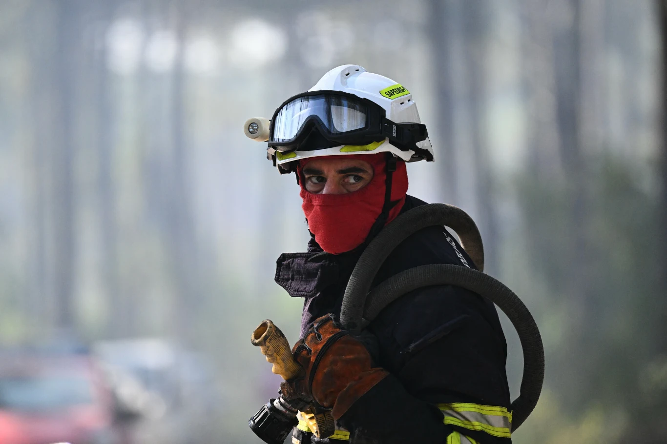 Francuscy strażacy walczą z pożarami w rejonie Żyrondy Strażak w hełmie i goglach ochronnych, z czerwoną kominiarką na twarzy, trzyma w rękach wąż strażacki, gotowy do akcji w lesie.