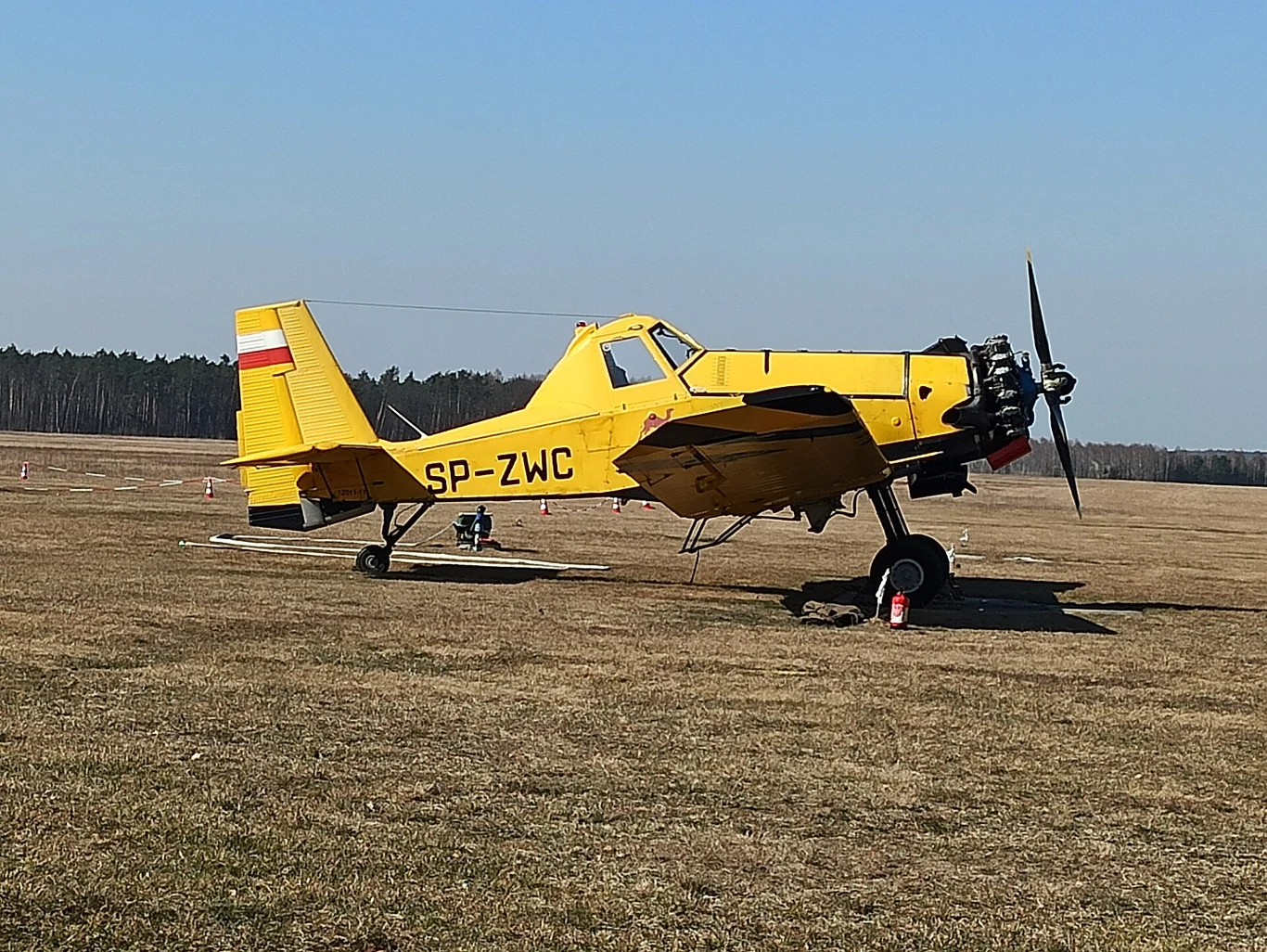 PZL P-18 Dromader na lotnisku Opole-Polska Nowa Wieś. Żółty samolot rolniczy typu PZL-Mielec M-18 Dromader stoi na trawiastym pasie startowym, w tle widoczny las i czyste niebo.