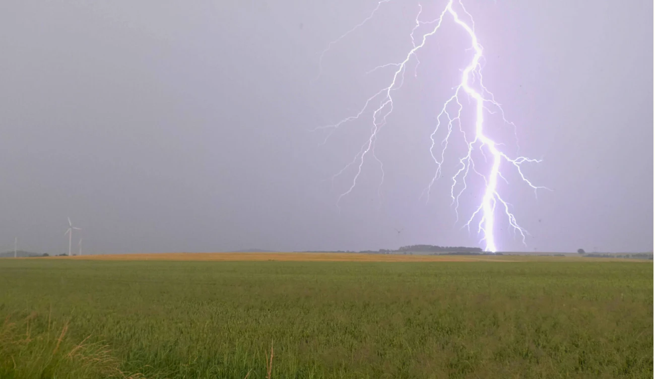 Czym jest sucha burza? Błyskawica nad polem, uderzająca w pobliżu horyzontu, z widoczną turbiną wiatrową po lewej stronie.