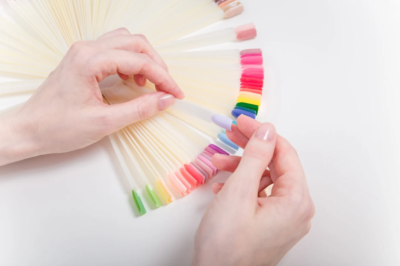 Jaki manicure powraca do mody? Ten rodzaj kilka lat temu był hitem Dłoń trzyma próbnik z różnokolorowymi wzornikami lakierów do paznokci w wachlarzu.