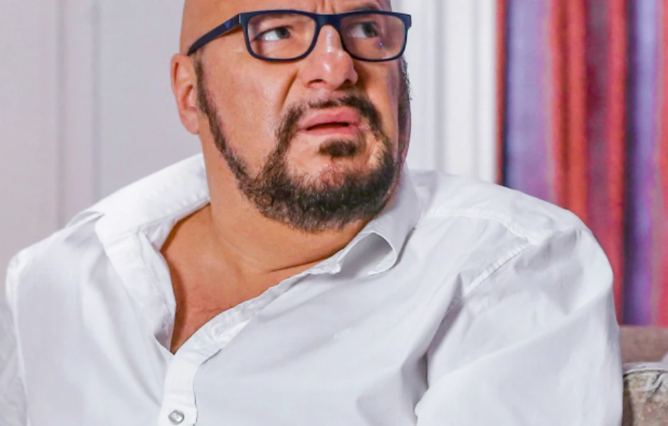 Łysy mężczyzna z brodą i okularami w białej koszuli patrzy z niepokojem w bok.