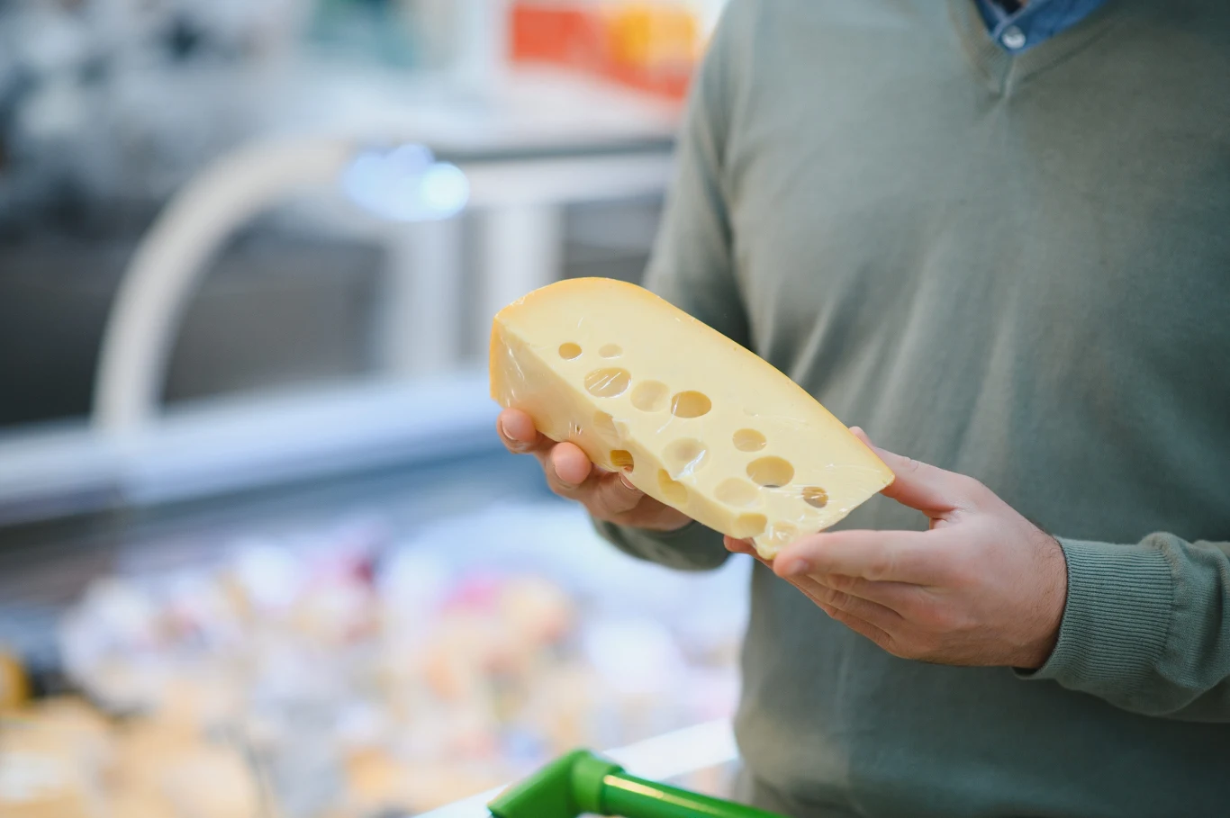 Dziury w serze żółtym to świetna wskazówka jakości. Warto dokładnie je obejrzeć. Mężczyzna trzyma kostkę żółtego sera z dziurami przy stoisku z nabiałem w sklepie.