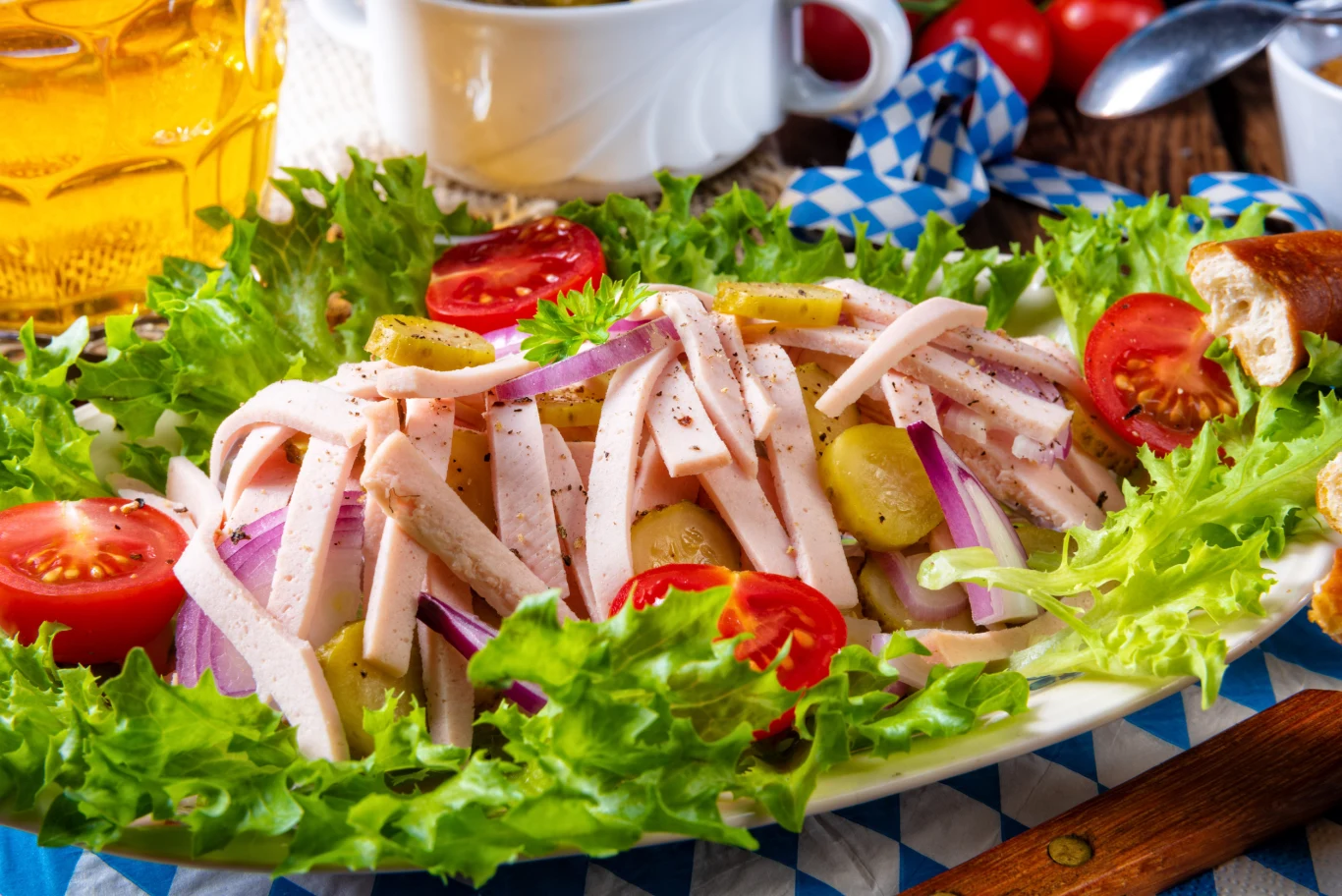 Sałatka bawarska doskonale sprawdzi się na grillach i rodzinnych imprezach Sałatka bawarska z paskami szynki, cebulą, ogórkami kiszonymi, pomidorem i sałatą na owalnym talerzu