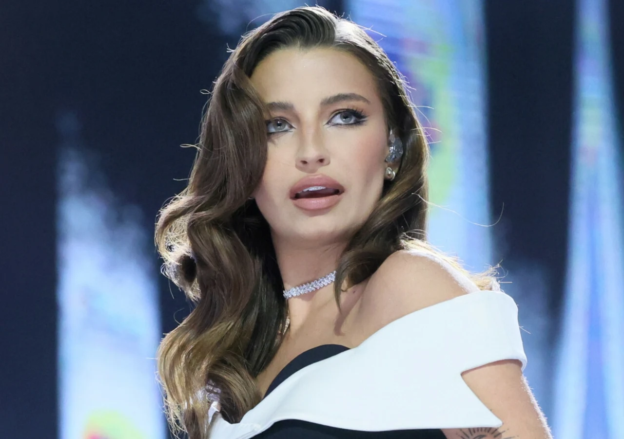 Julia Wieniawa Julia Wieniawa w eleganckiej, czarno-białej sukni i błyszczącym naszyjniku. Stoi na scenie z przejętym wyrazem twarzy.