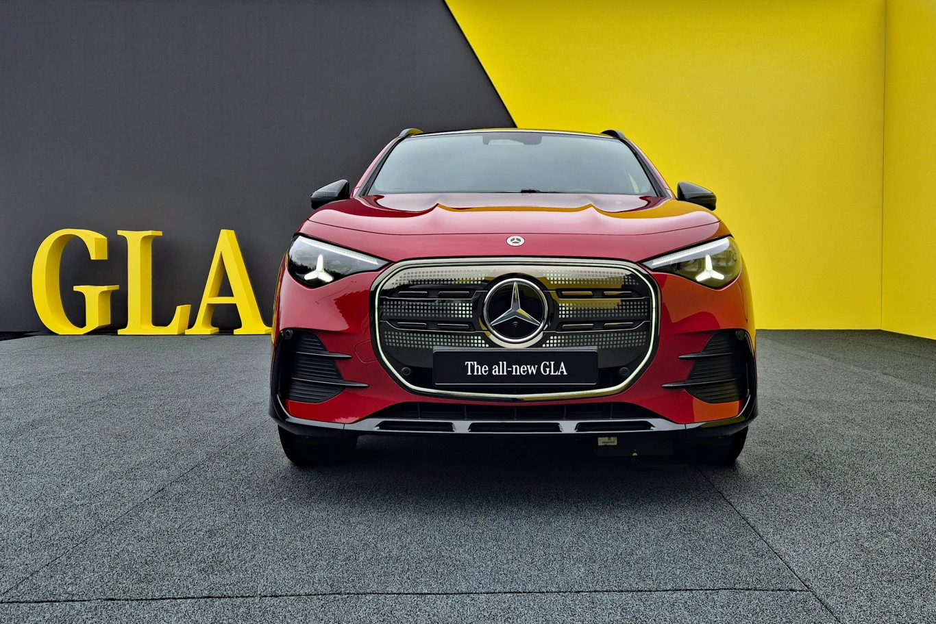 Czerwony Mercedes GLA z nowoczesnym przednim grillem ustawiony na tle kontrastowej żółto-czarnej ściany z dużymi literami GLA.